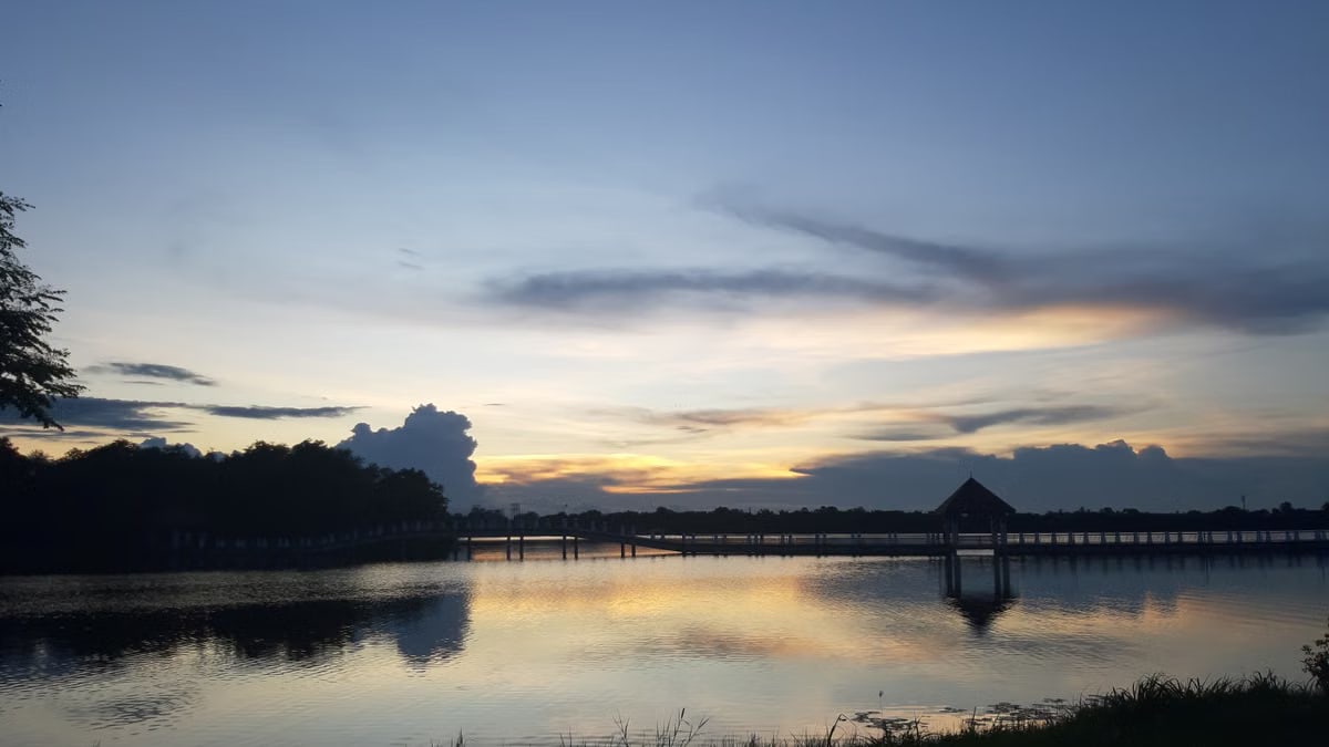 Peaceful dusk over a Thai lake with reflections and a bridge.