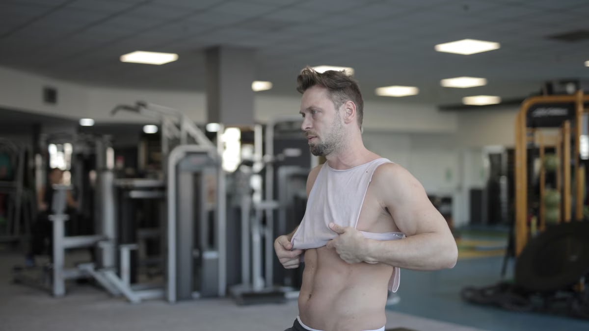 Side view of tired male athlete with muscular body standing in sports center after training while relaxing and looking away